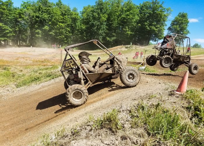 2 dirt buggies racing over a hill on a sunny day