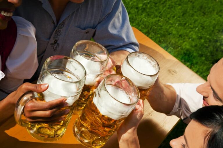 4 Steins of beer on a tray outside people grabbing them